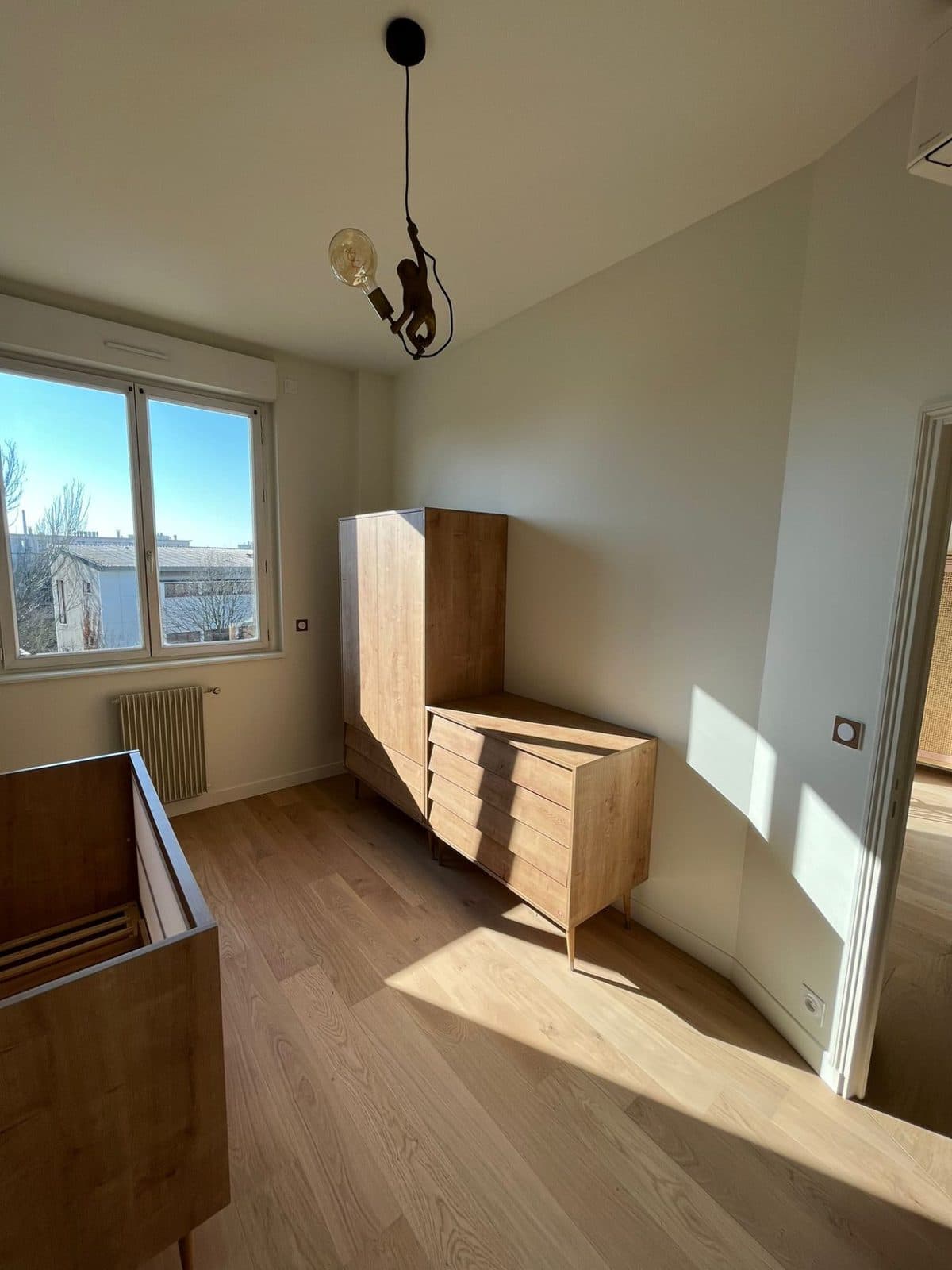 Chambre de bébé : armoire et commode en bois, suspension singe, parquet chêne au soleil