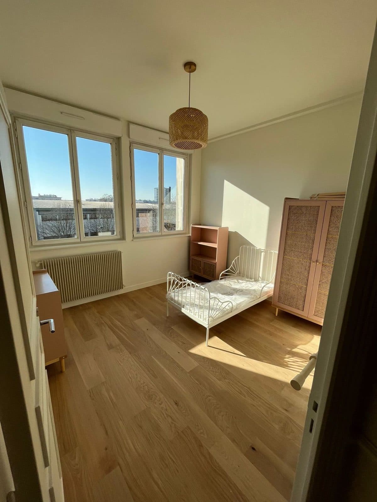Chambre d'enfant : deux fenêtres, armoire en cannage rose, lit en métal blanc