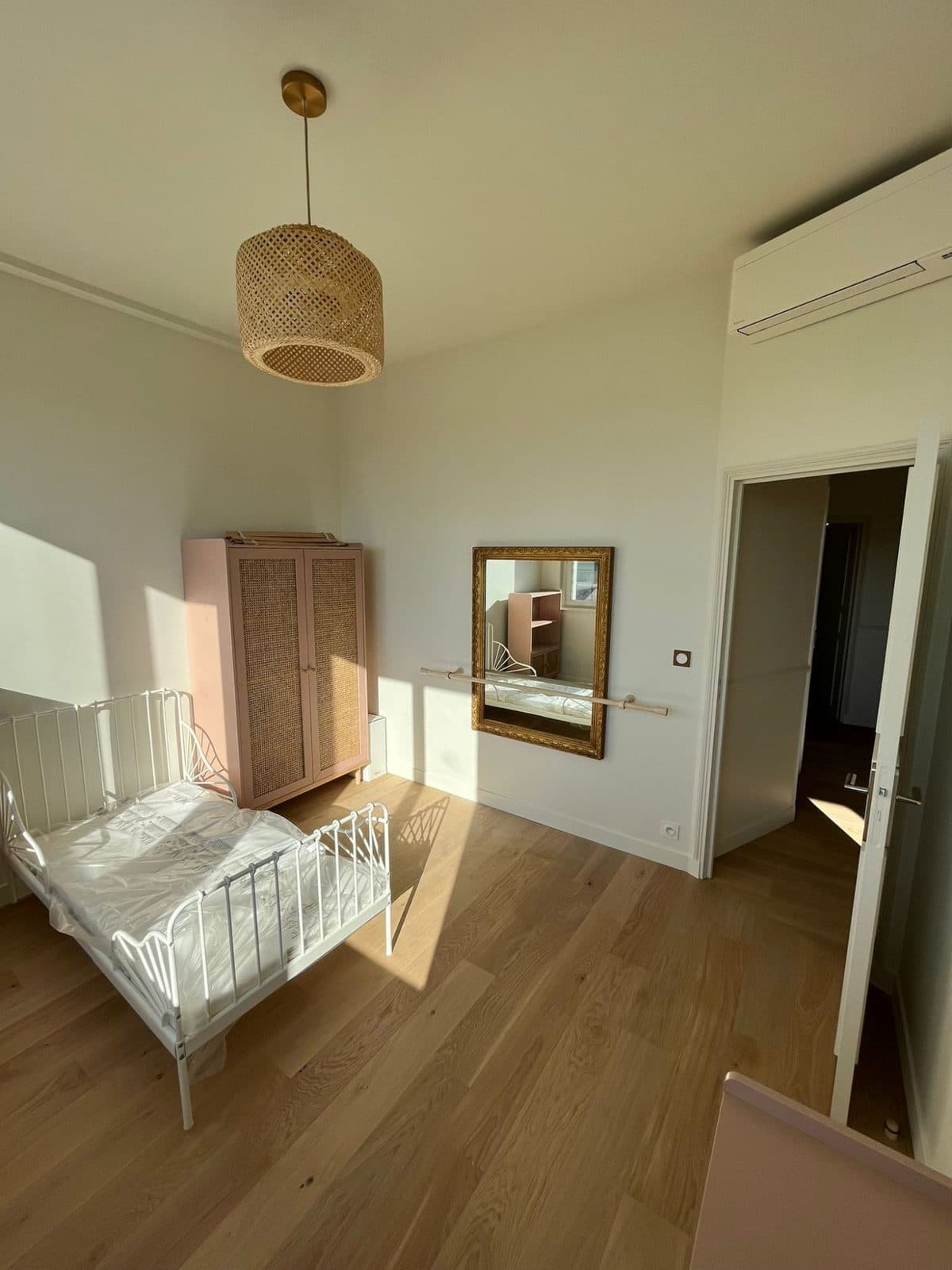 Chambre d'enfant lumineuse : armoire rose en cannage, lit en métal blanc, suspension en rotin