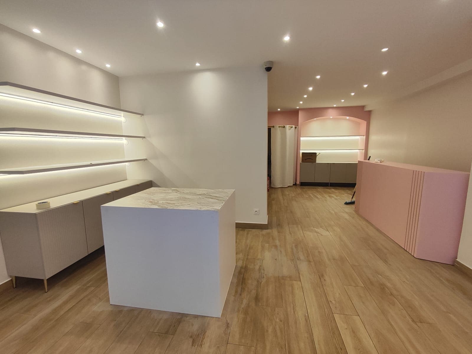 Local commercial aménagé : étagères rétroéclairées, meubles bas, îlot à plateau marbré et comptoir rose