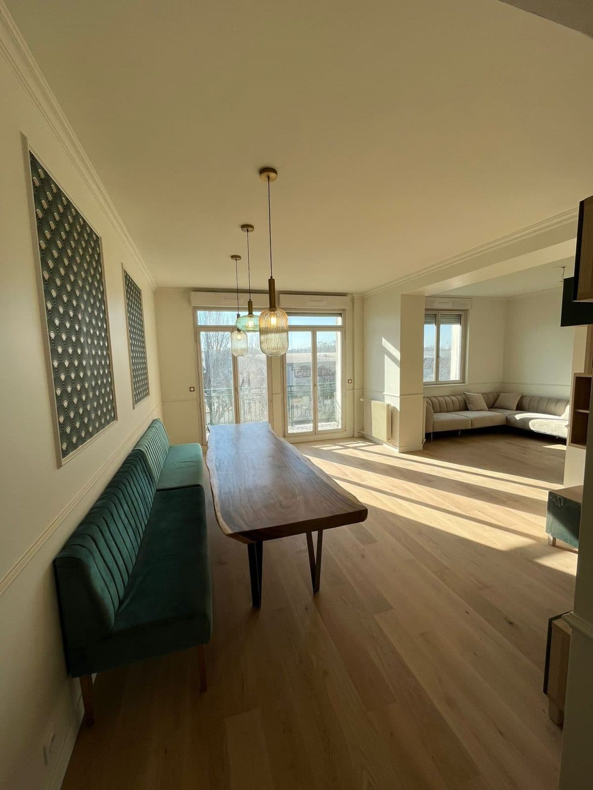 Salle à manger : banquette en velours vert, table en bois brut, panneaux décoratifs et grandes portes-fenêtres