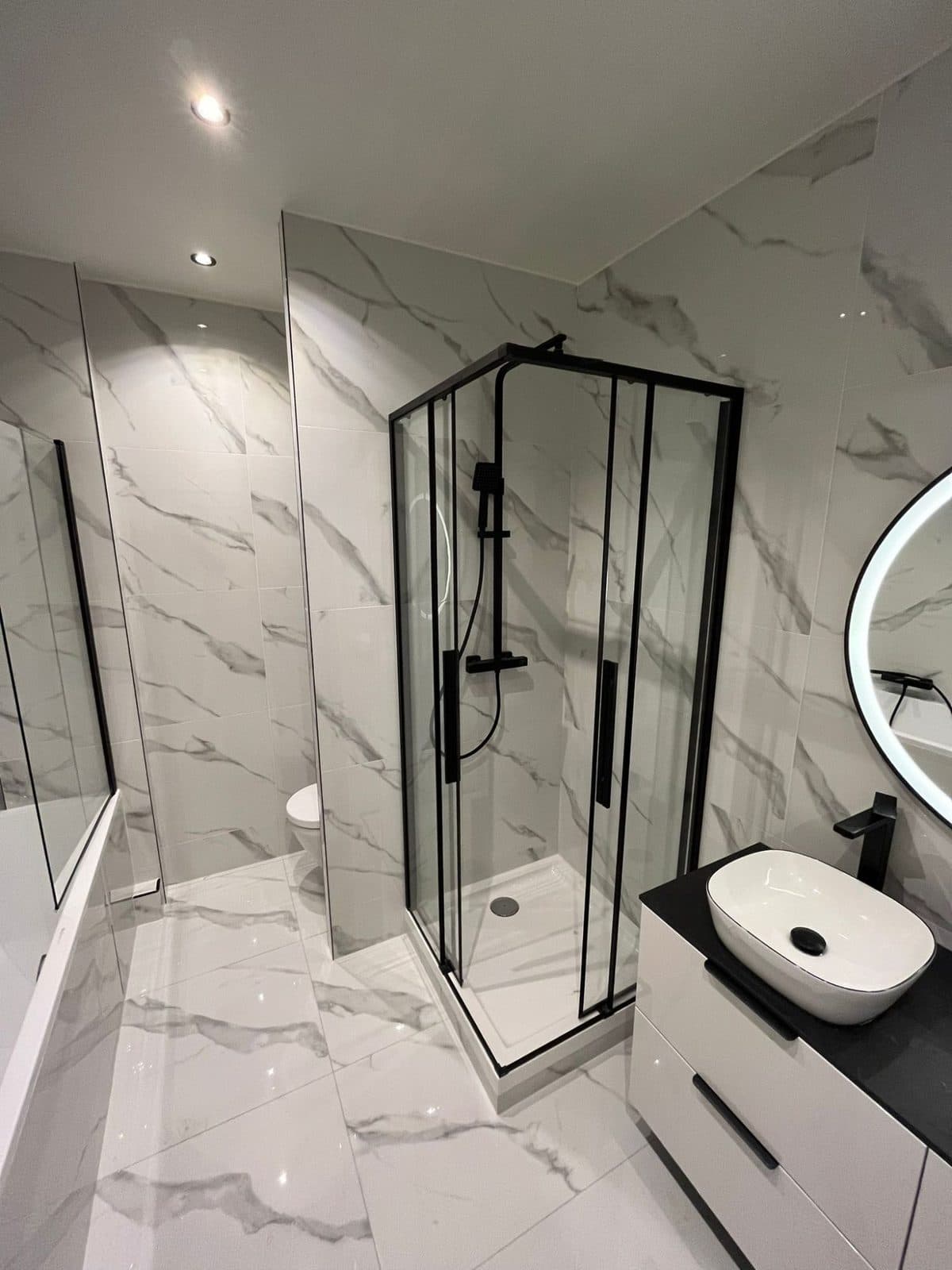 Salle de bain : douche d'angle à profilés noirs, vasque à poser et grès effet marbre