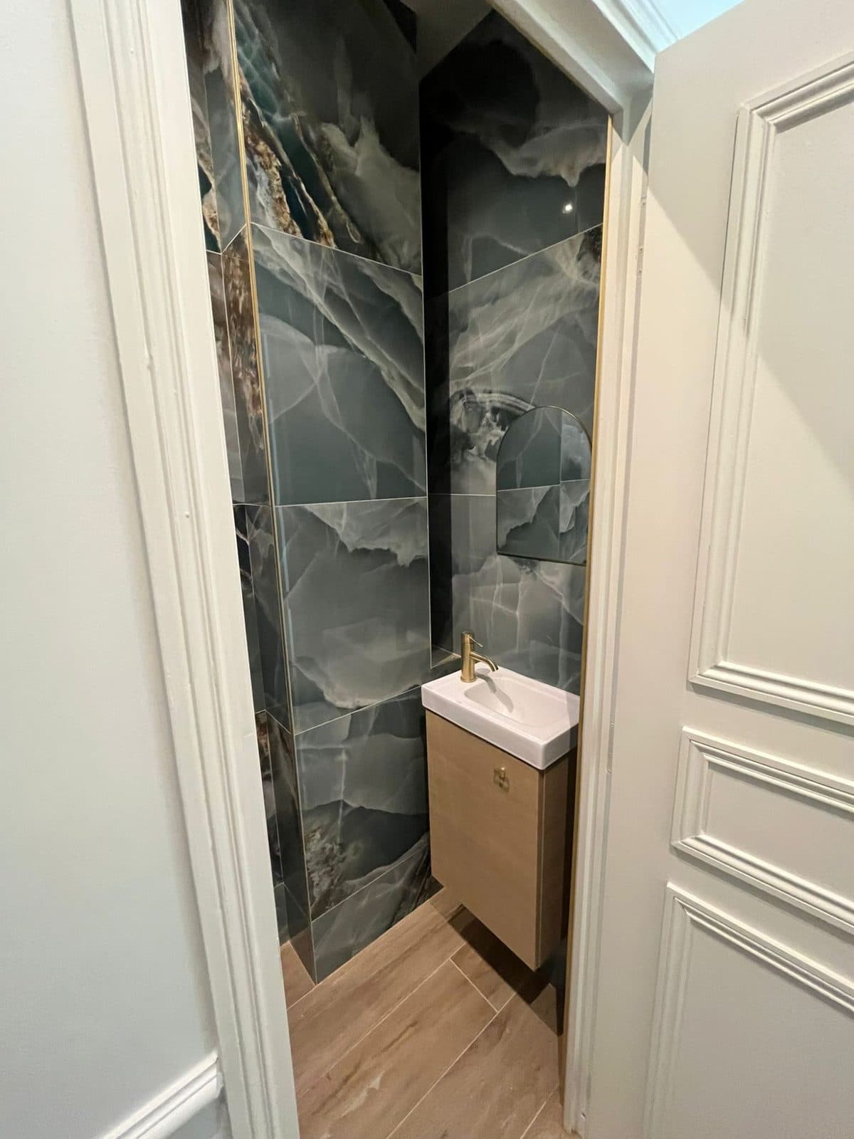 WC habillé de grands carreaux effet onyx vert, profilés laiton, lave-mains sur meuble bois et robinet doré
